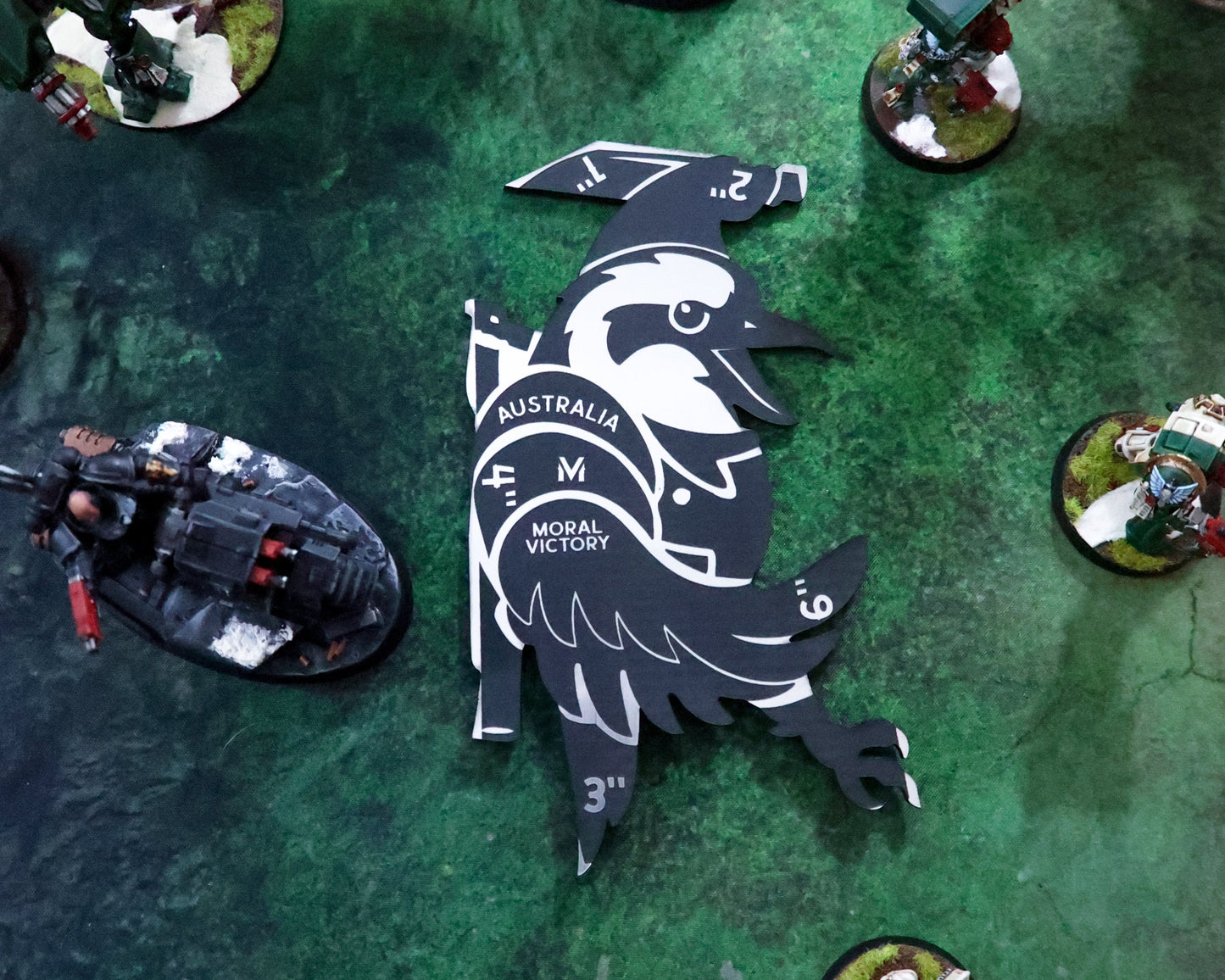 Miniature gaming figures on a green playing field with a large black and white emblem.