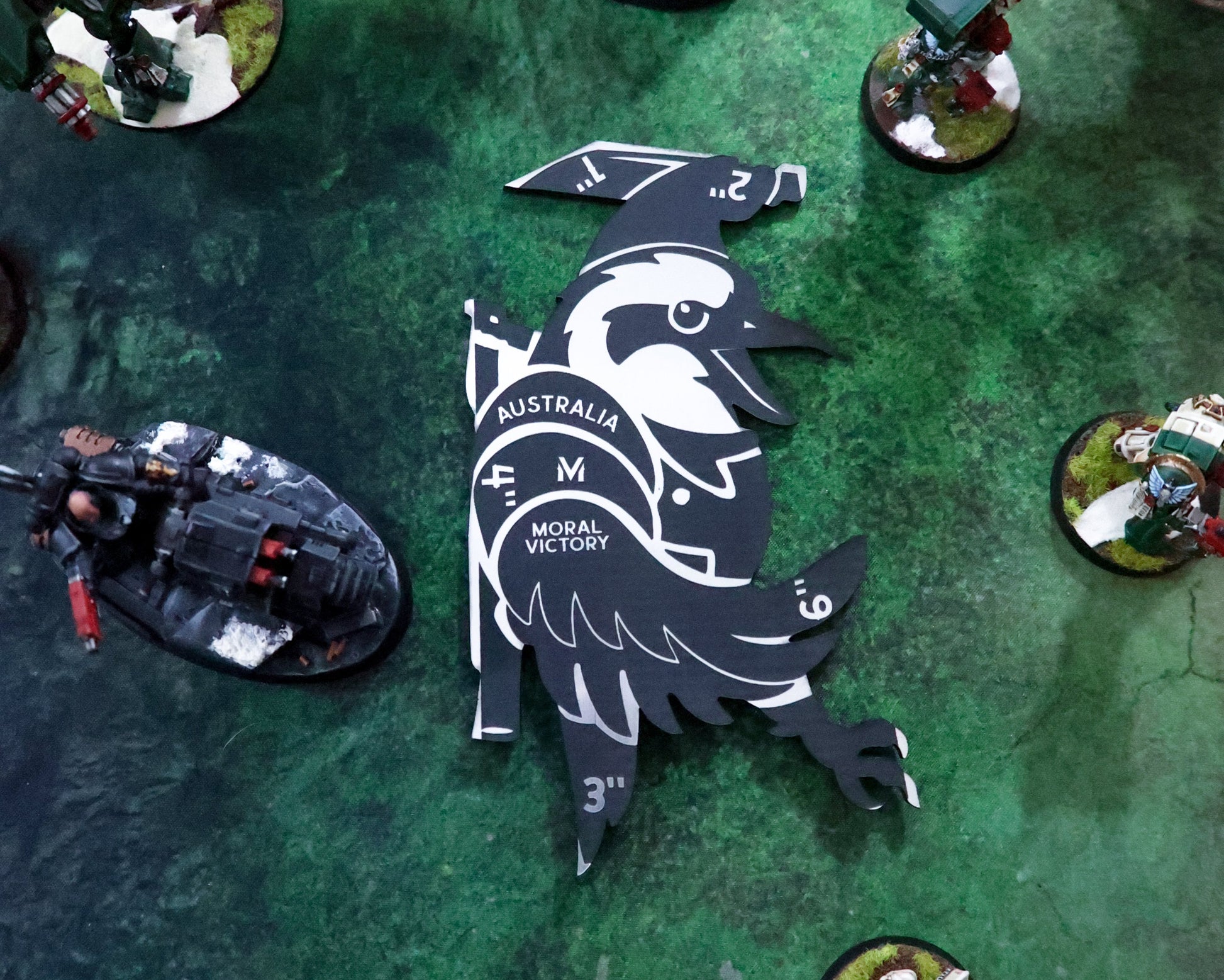 Miniature gaming figures on a green playing field with a large black and white emblem.